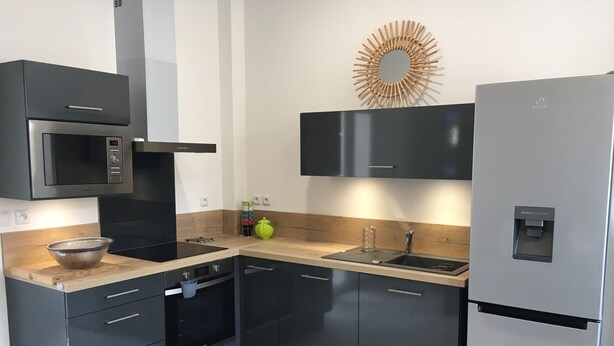 Eine moderne Küche mit integriertem Mikrowellenherd, Backofen und Kühlschrank. Es gibt ein Waschbecken mit Armatur, eine Holz Arbeitsplatte und einen dekorativen Spiegel darüber.