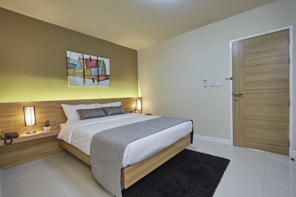 A modern bedroom with a large bed, bedside tables, a wooden door, and a wall-mounted abstract art piece.