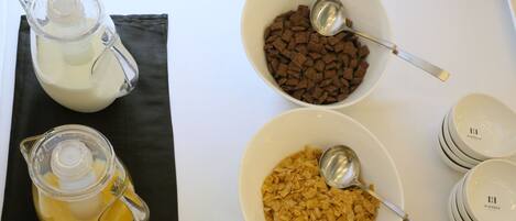 A table with three bowls containing different food items, a pitcher of milk, and a stack of bowls.