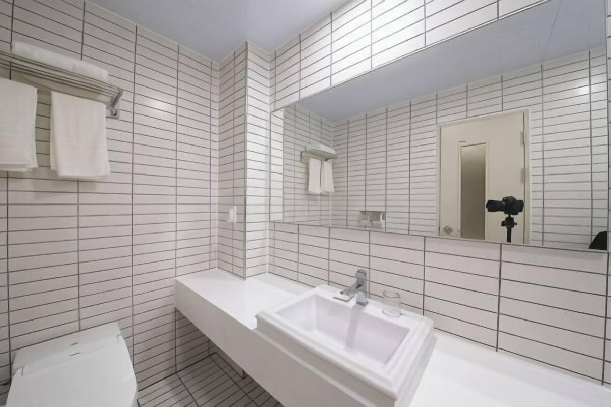 Ein modernes Badezimmer mit weiß gefliesten Wänden, einem weißen Waschbecken und einem großen Spiegel.