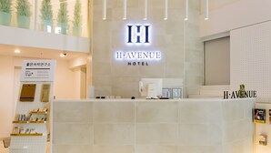 A reception desk at the H. Avenue Hotel with a modern design, featuring a prominent illuminated sign and a digital display. - H Avenue Hotel Idae Shinchon (Seoul)