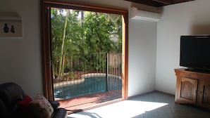 A living room with a sliding glass door leading to a pool, a television, and a wooden cabinet. - Beach House on Fox (Cable Beach)