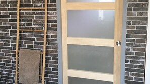 Et rum med en trædør med frostet glas, en træstige lænet mod en murstensvæg, og en gulvtæppe med et mønster på gulvet.
