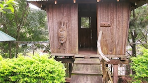 Una casa del árbol de madera con techo metálico, una escalera de madera y un cartel que dice "Bantoc".