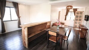 Un comedor moderno con un banco y una mesa de madera, un jarrón con flores y vistas al exterior a través de amplias ventanas.