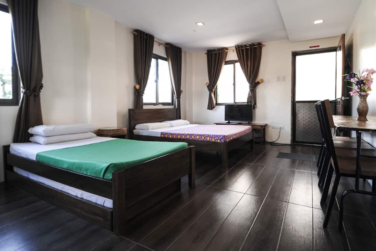 A hotel room with two wooden beds, a desk with a chair, a television, and a window with curtains.