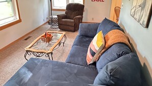 A living room with a blue sectional sofa, a small coffee table, a chair, and a wall with a motivational quote.