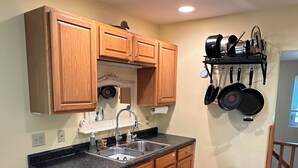 A kitchen with wooden cabinets, a granite countertop, a stainless steel sink, and a hanging pot rack.