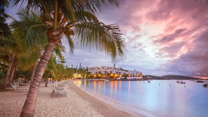 A beachfront hotel with a sandy beach, palm trees, and a calm sea. -   Spacious 3 Bed 3 Full Baths With Spectacular Views of St John- Ocean Front!
 (Saint Thomas)