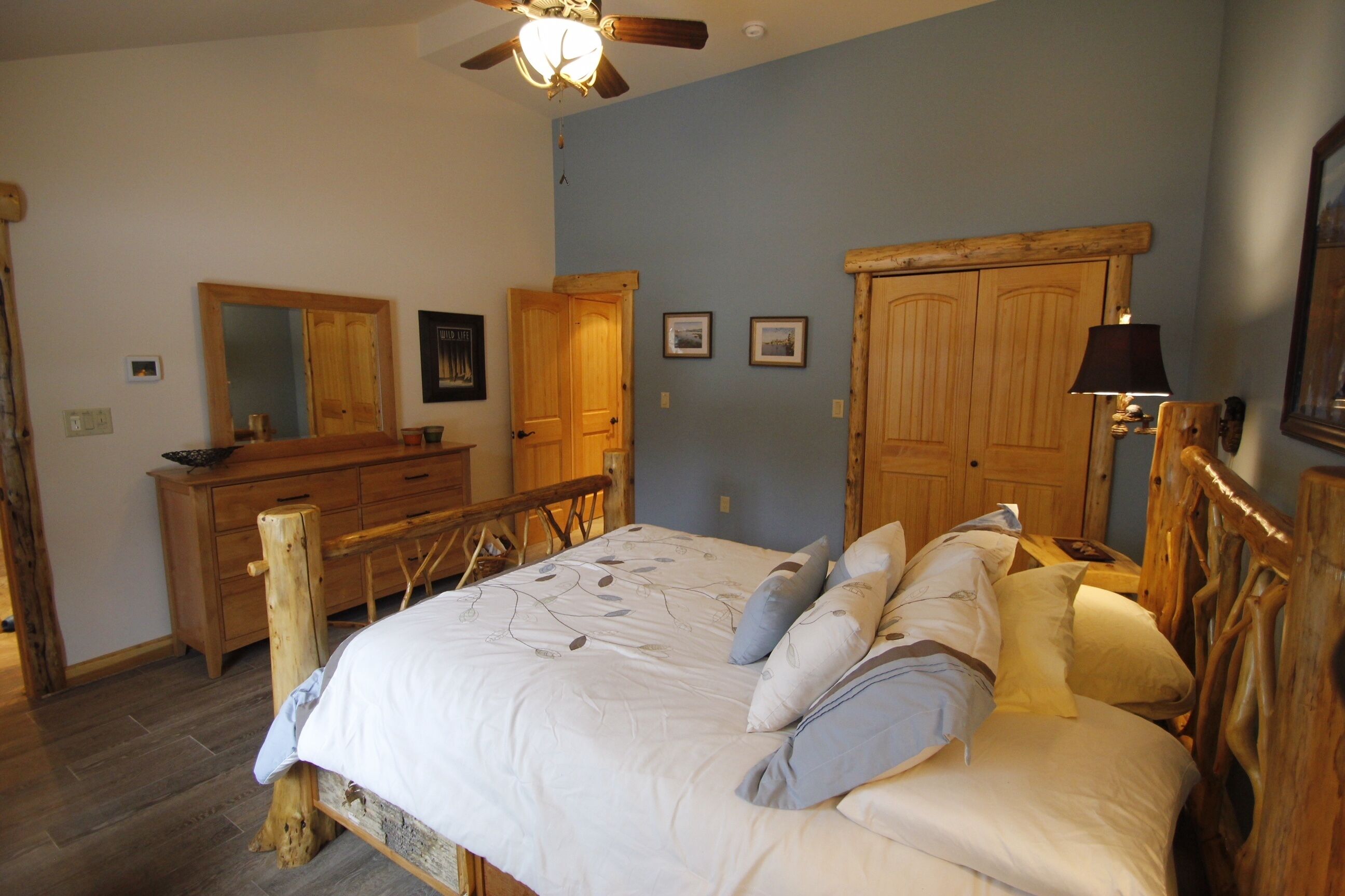 Un dormitorio con estructura de cama de madera, cómoda, espejo y ventilador de techo.