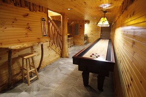 A wooden room with a pool table, stools, and a wooden bar.