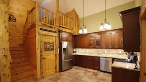 A kitchen with wooden cabinets, a stainless steel refrigerator, and a wooden staircase.