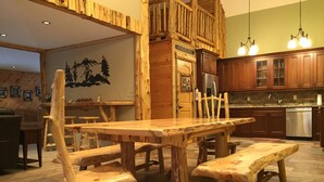 A rustic wooden dining area with a large table and benches, a kitchen with wooden cabinets, and a wall with a mountain mural.