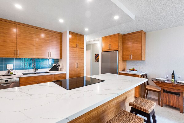 A modern kitchen with wooden cabinets, a stainless steel refrigerator, and a marble countertop.
