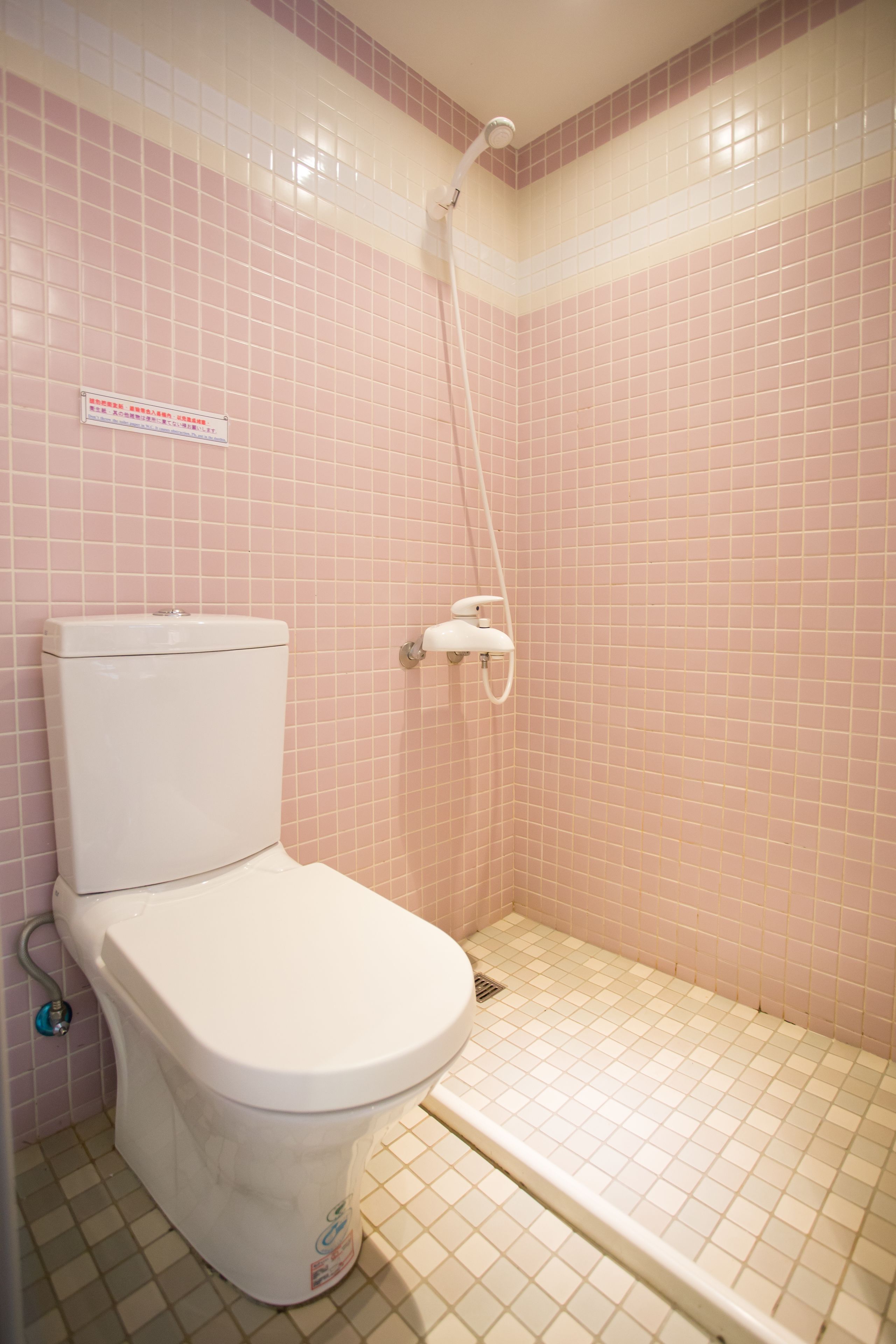 Un baño con inodoro, ducha y paredes con azulejos rosa.