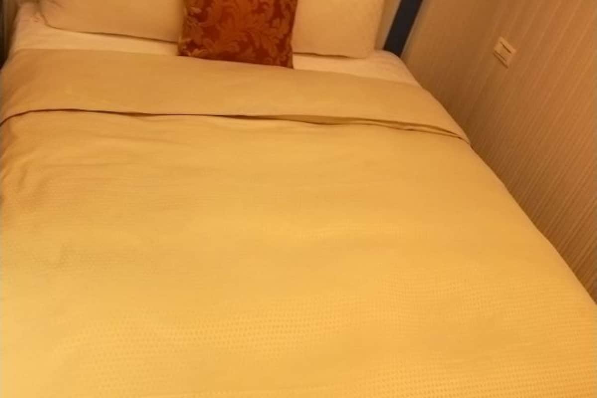 A bed with a beige bedspread and a patterned pillow.