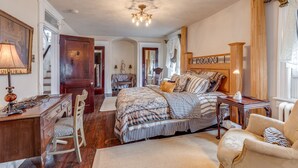 A spacious bedroom with a large bed, a desk, and a chair. There is a chandelier on the ceiling and a window with curtains. - Victorian Home - Golfers Welcome (Ventnor)