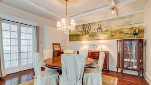 A dining room with a round table, chairs, a chandelier, a painting, and a cabinet. - Victorian Home - Golfers Welcome (Ventnor)