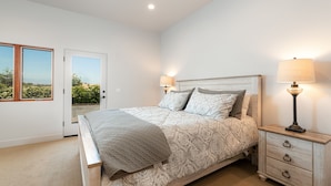 Ein Schlafzimmer mit einem Bett, zwei Nachttischlampen, einem Nachttisch und einer Tür zu einem Balkon.