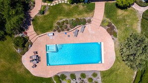Luftaufnahme eines Schwimmbeckens mit einer Terrassenanlage, umgeben von Rasen und Bäumen.