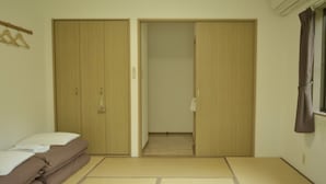 A room with a futon bed, a wooden wardrobe, and a sliding door leading to a hallway. - Yakushima Guesthouse Suginoko (Yakushima)