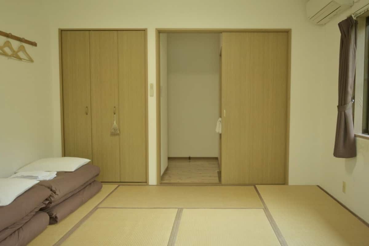 A room with a futon bed, a wooden wardrobe, and a sliding door leading to a hallway.