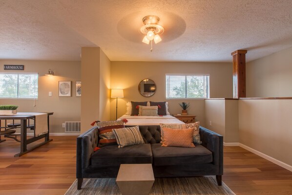 A cozy bedroom with a bed, a dark sofa, a small table, and a ceiling fan.