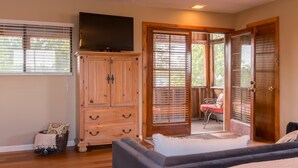 A bedroom with a large wardrobe, a flat-screen TV, a sofa, and a sliding glass door leading to a patio with a chair. - Gorgeous Casita In The Heart Of Historic Old Town  (Albuquerque)
