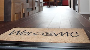 A hallway with a 'Welcome' mat leading to a dining area with a high ceiling and natural light. - YAWP! backpackers - Hostel (Tokyo)