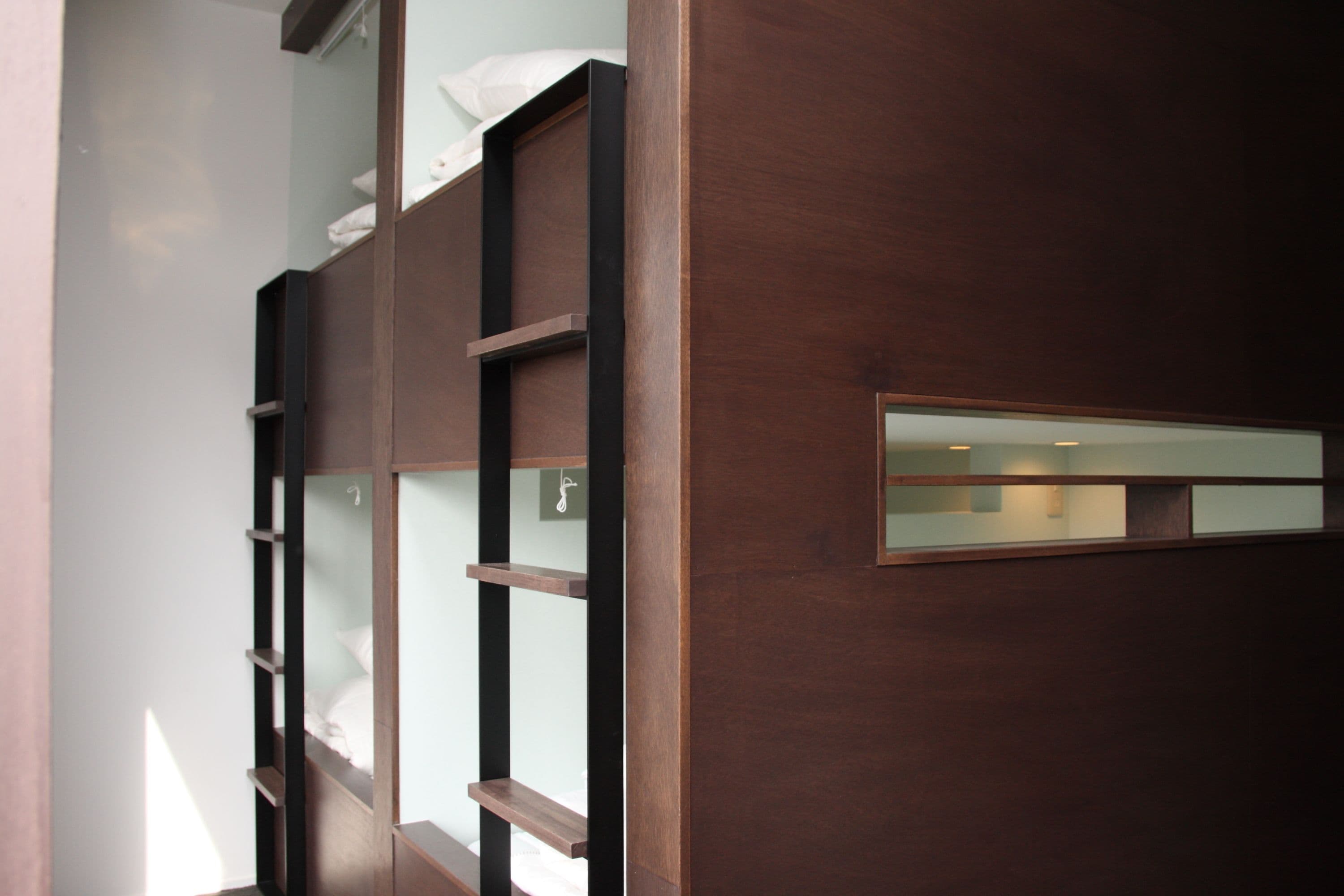 A modern, multi-level wooden bunk bed with built-in shelves and a small mirror.