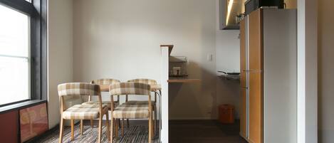 A compact kitchen with a refrigerator, a dining area with chairs, and a window providing natural light.