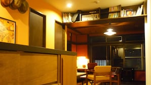 A cozy room with wooden cabinets, a dining table with chairs, a bookshelf, and a window with a view of the outside. - YAWP! backpackers - Hostel (Tokyo)
