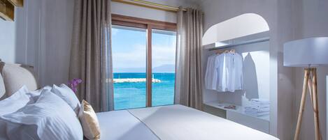 A hotel room with a bed, a view of the sea, a wardrobe, and a desk with a lamp.
