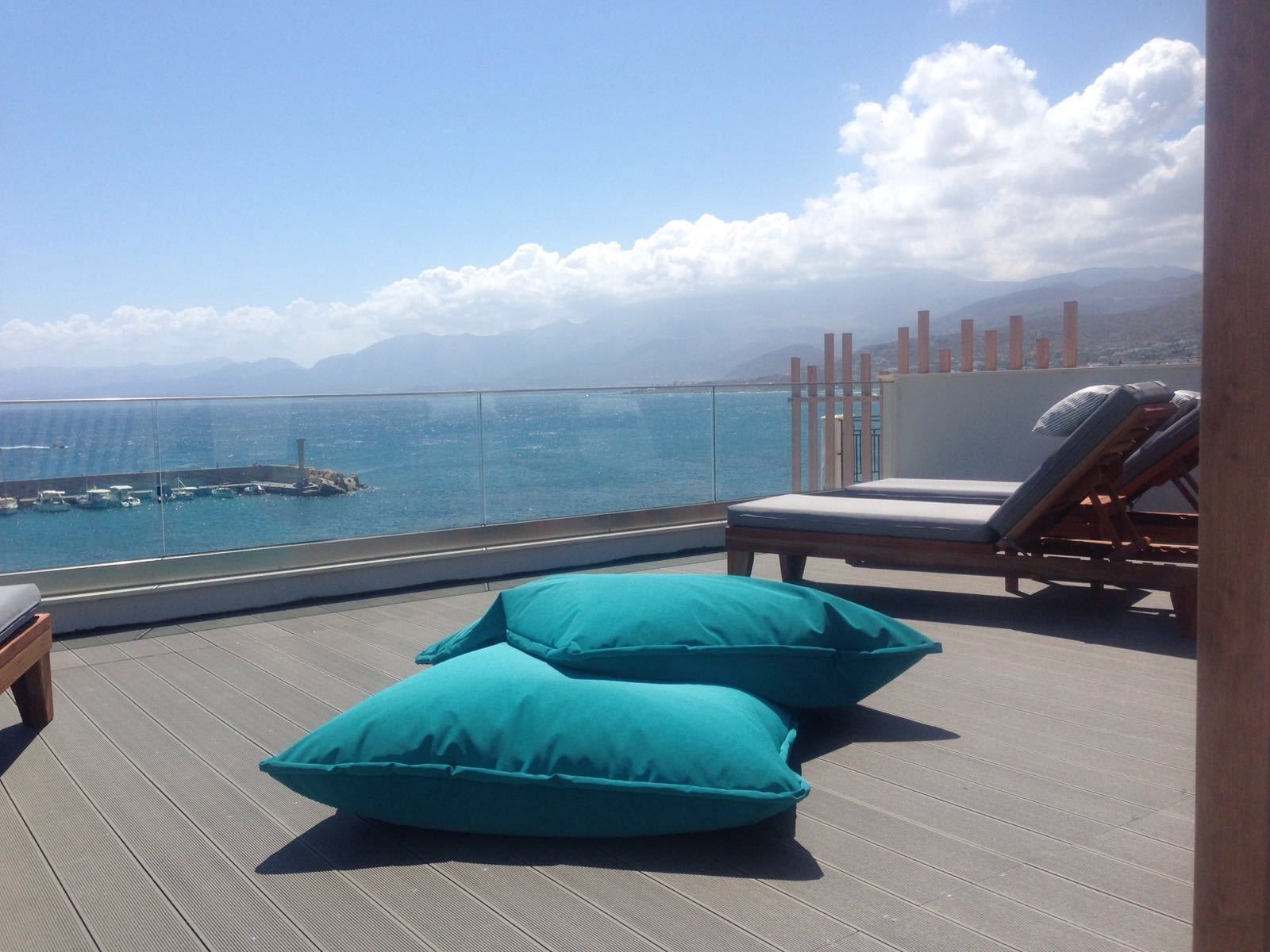 A balcony with a view of the sea, a lounge chair, and two teal cushions.
