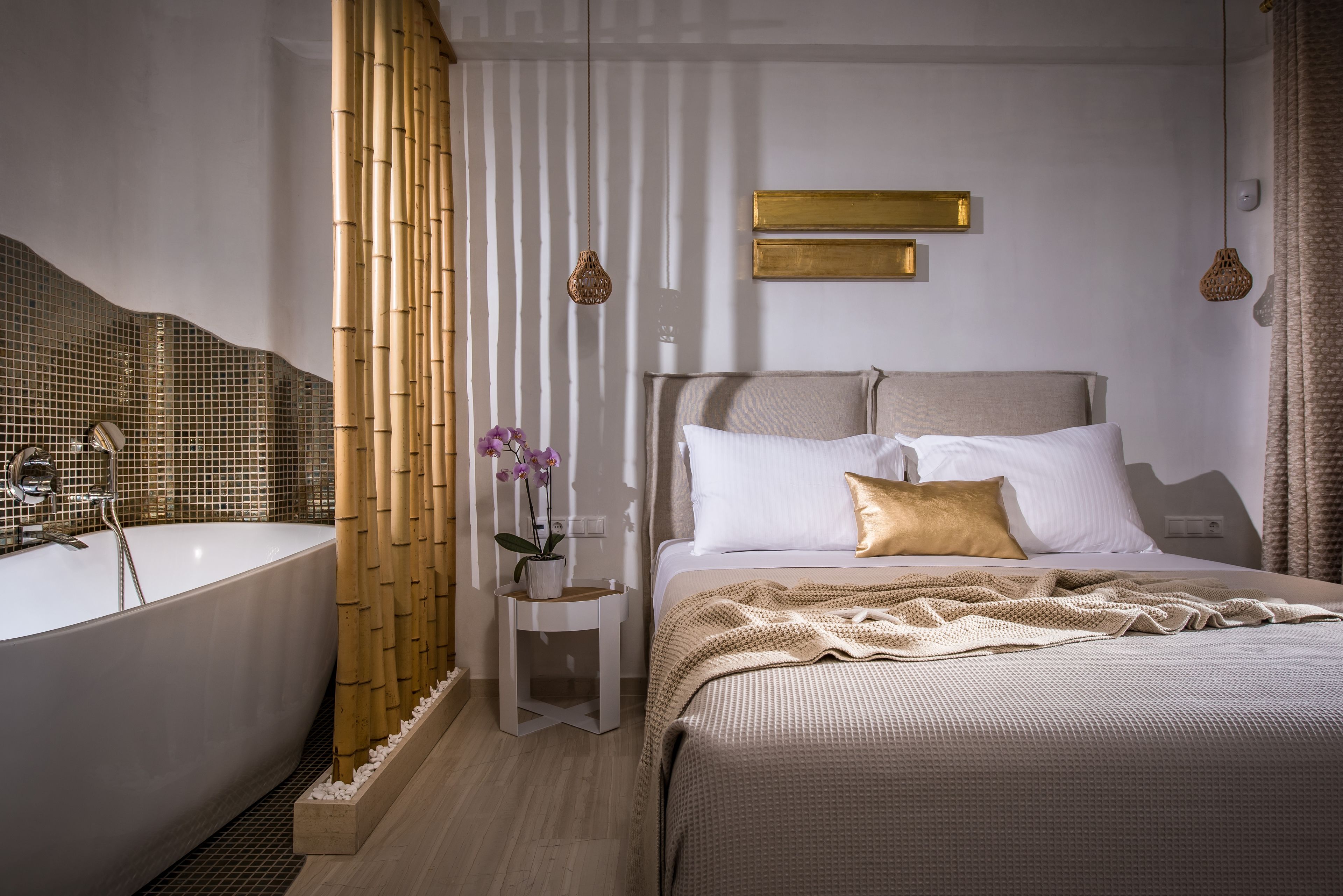 Une chambre moderne avec une grande baignoire, une table de chevet agrémentée d’une plante et un lit avec un oreiller doré.