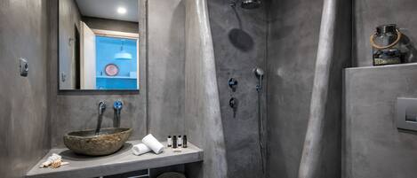 Une salle de bain moderne avec un grand lavabo en pierre de forme ronde, un miroir et une douche au design incurvé.