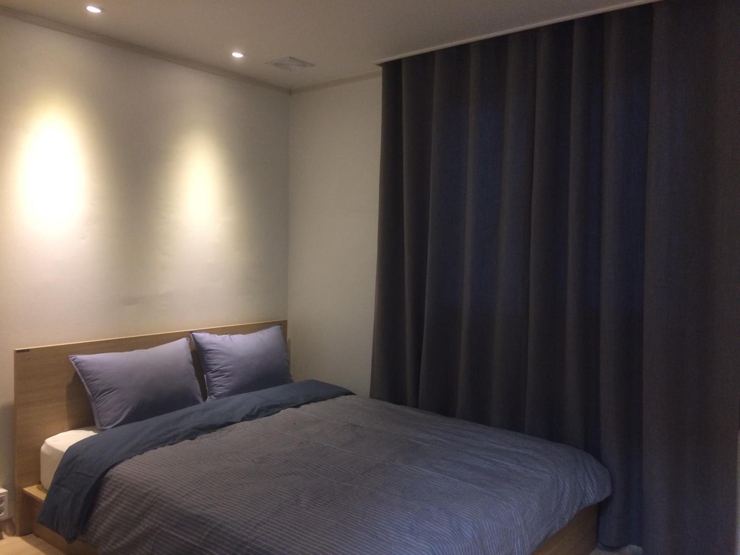 Quarto moderno com cama, cortinas escuras e luminária fixada na parede.