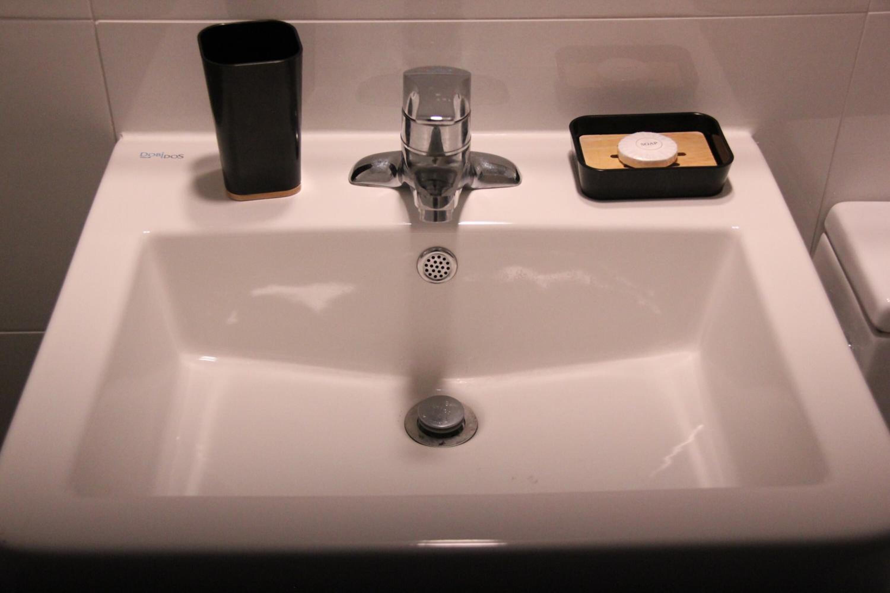 A bathroom sink with a soap dispenser, a soap dish, and a trash bin.