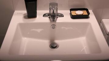 A bathroom sink with a soap dispenser, a soap dish, and a trash bin.