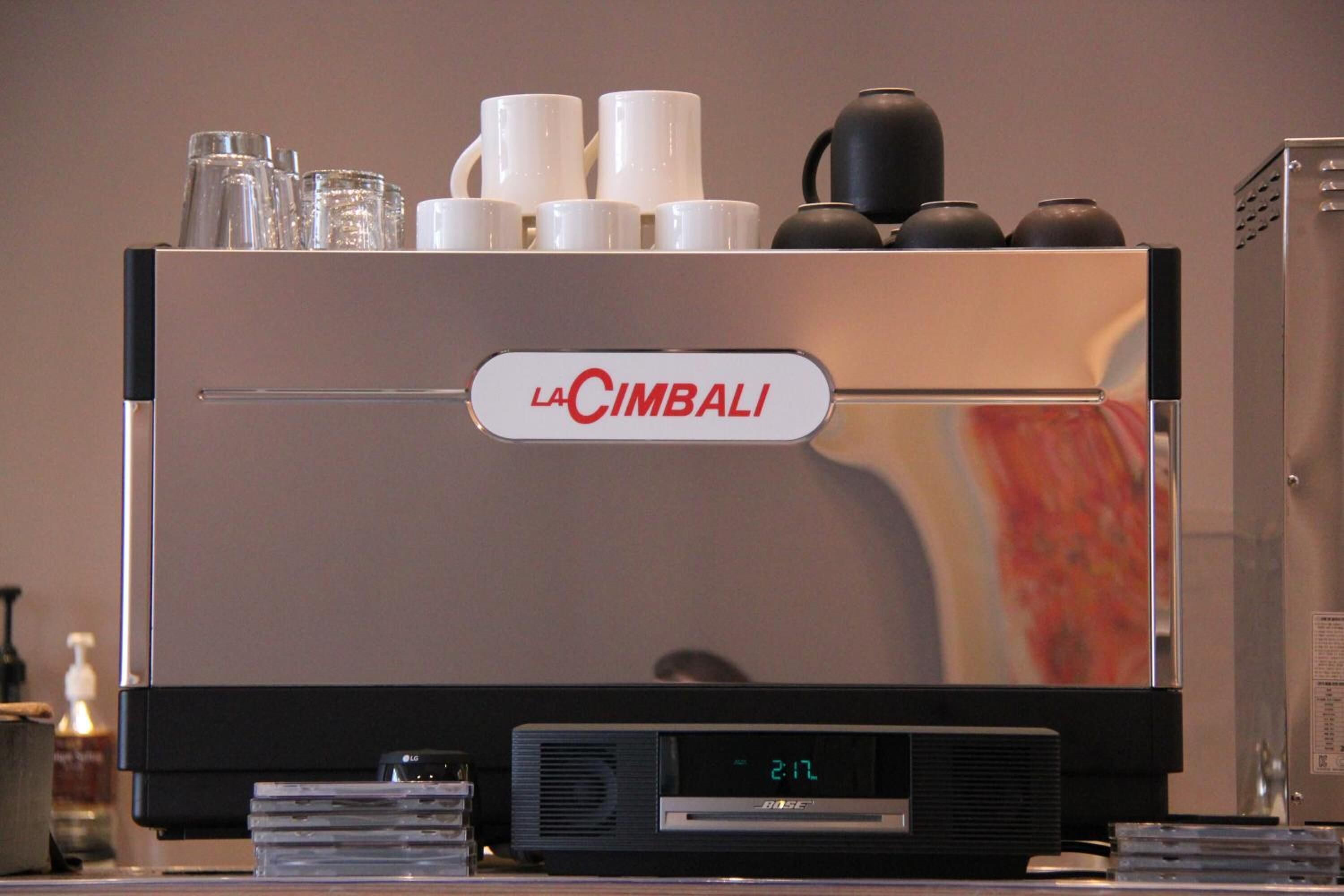 Una máquina de espresso La Cimbali con pantalla digital, tazas y un hervidor encima.