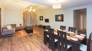 Una sala moderna con sofá, mesa de comedor preparada para cuatro personas y un amplio ventanal con cortinas.