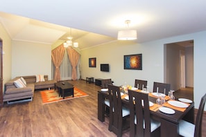 A modern living room with a sofa, dining table set for four, and a large window with curtains.