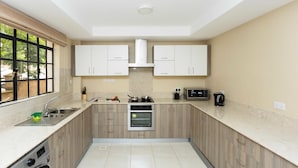 Una cocina moderna con lavadora integrada, horno y microondas. Cuenta con armarios de madera clara, un ventanal amplio y una encimera color beige.