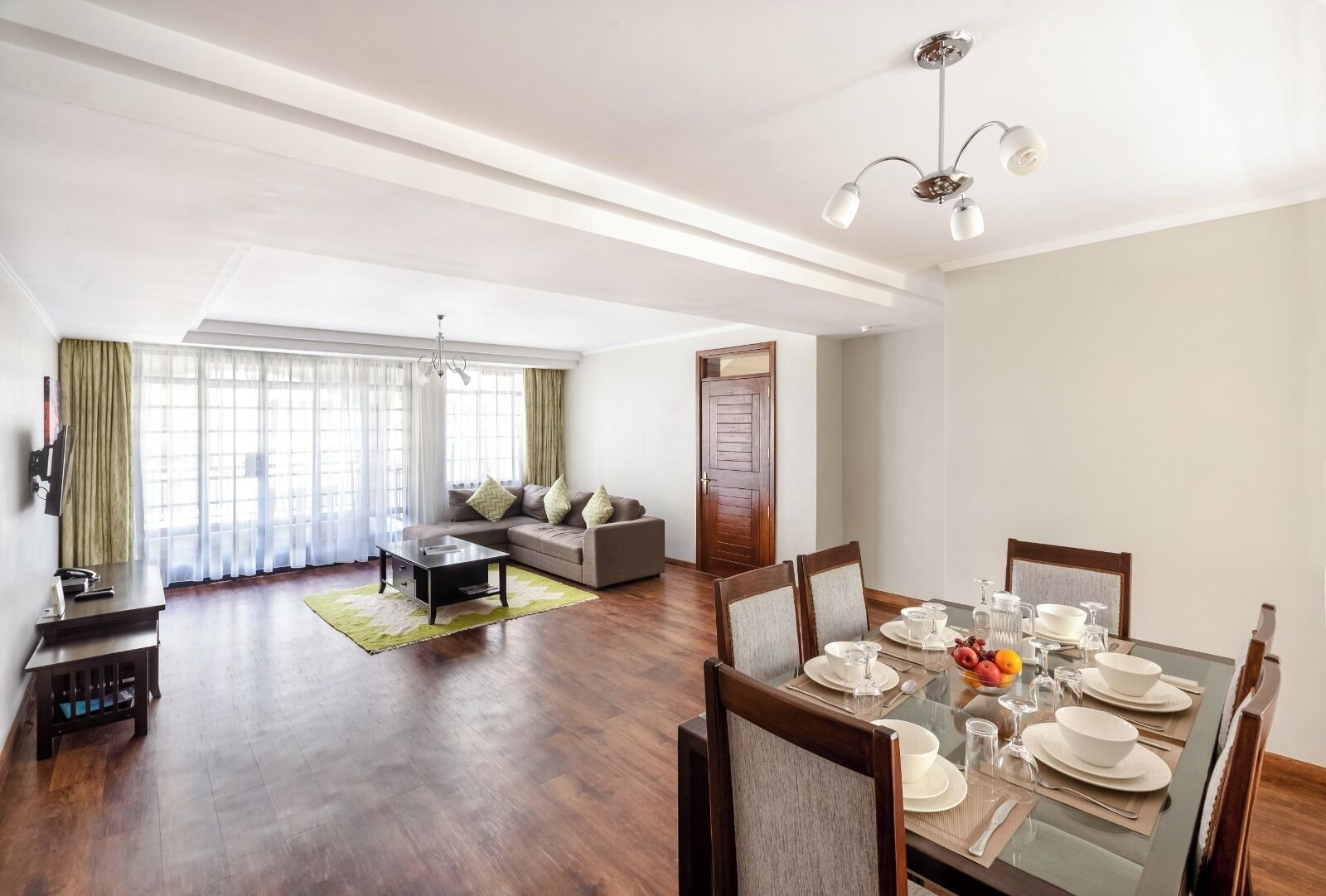 A spacious living area with a dining table set for four, a sofa, and a television.