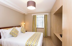 A hotel room with a bed, a wardrobe, a window with curtains, and a pendant light. - Cozy Residences (Nairobi)
