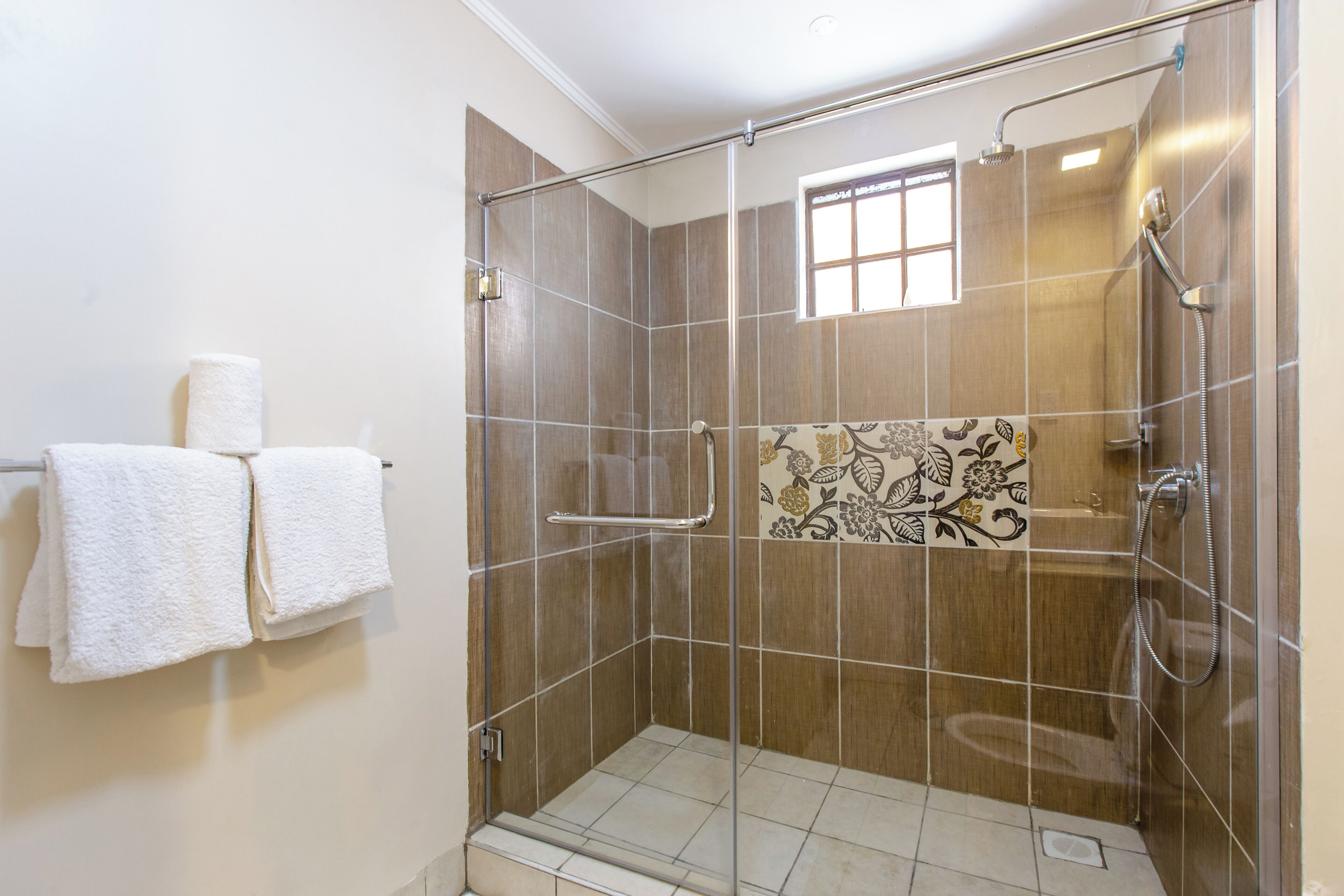 Une douche fermée par des parois de verre, avec un sol carrelé et une fenêtre.