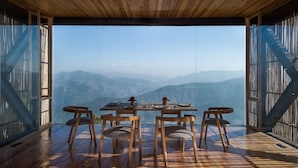 Ein Essbereich mit Tisch für vier Personen, umgeben von Holzstühlen, mit Blick auf eine gebirgige Landschaft durch große Glasfenster.