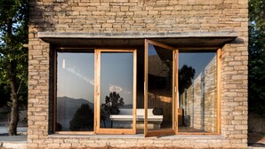 Ein modernes Haus mit Natursteinfassade, großen Glasfenstern und einer Holzterrasse.
