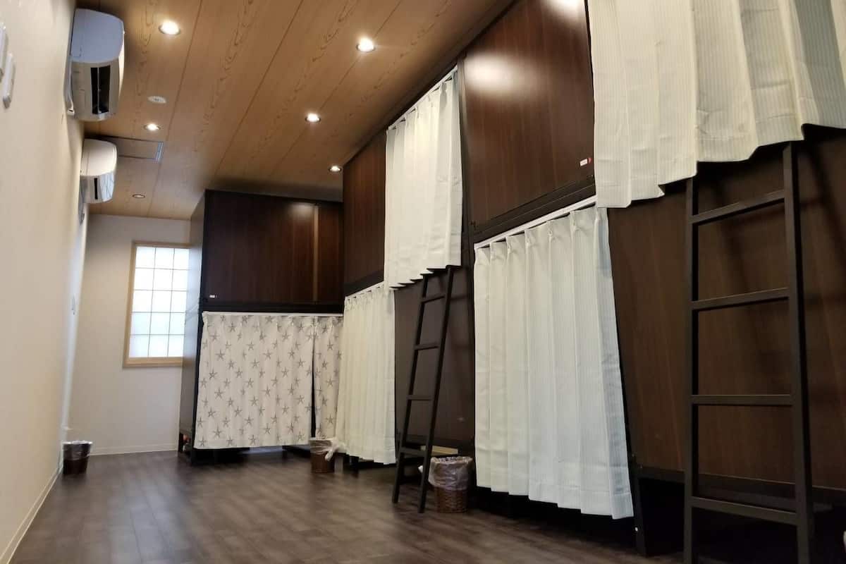 Ein Zimmer mit Holzboden, einem Fenster mit Vorhängen mit Sternenmuster, einer Leiter und einer weißen Klimaanlage an der Wand.