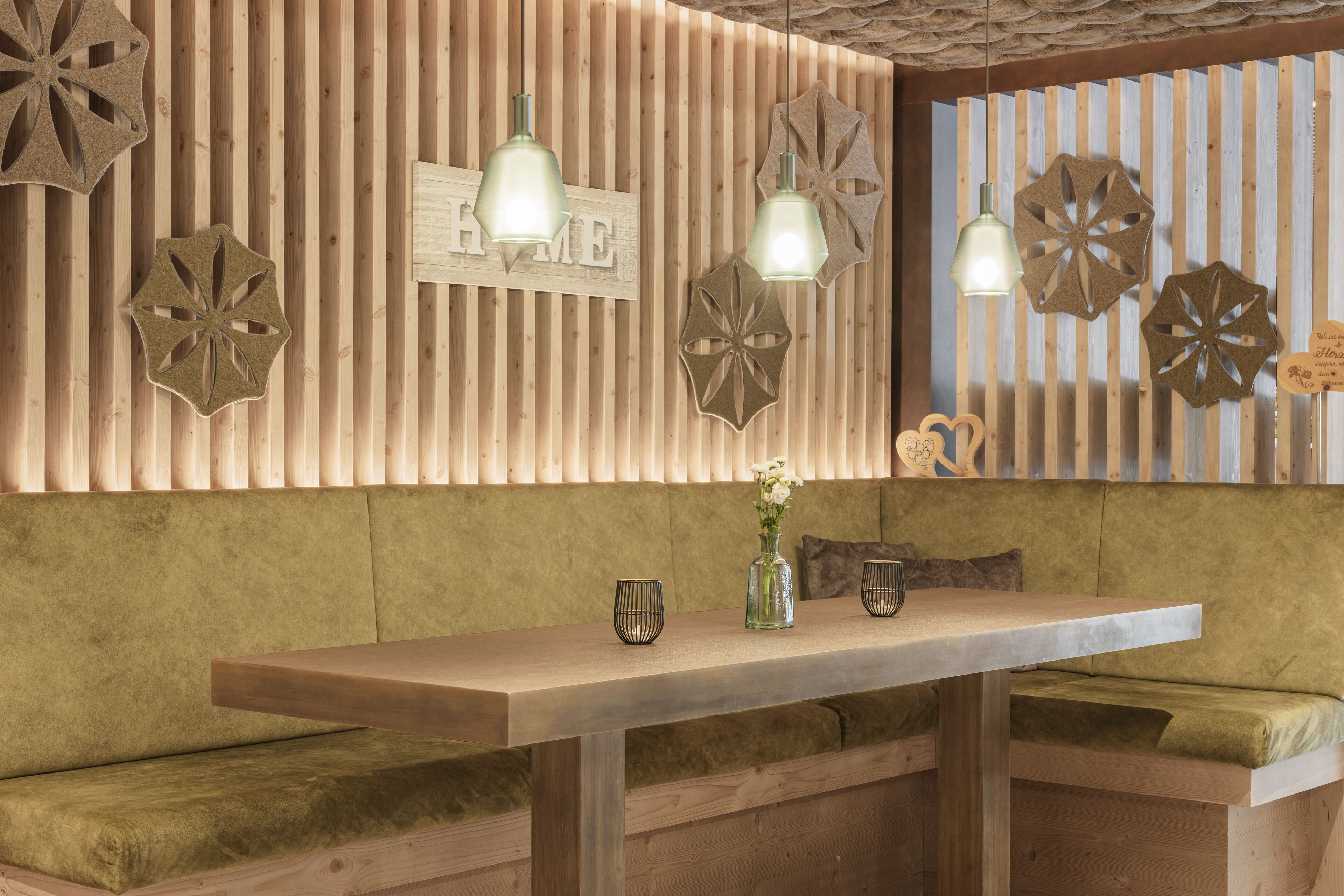 Eine hölzerne Bank mit gepolstertem Sitz, ein Holztisch mit zwei Gläsern und einer Vase, und dekorative Wandverkleidungen.